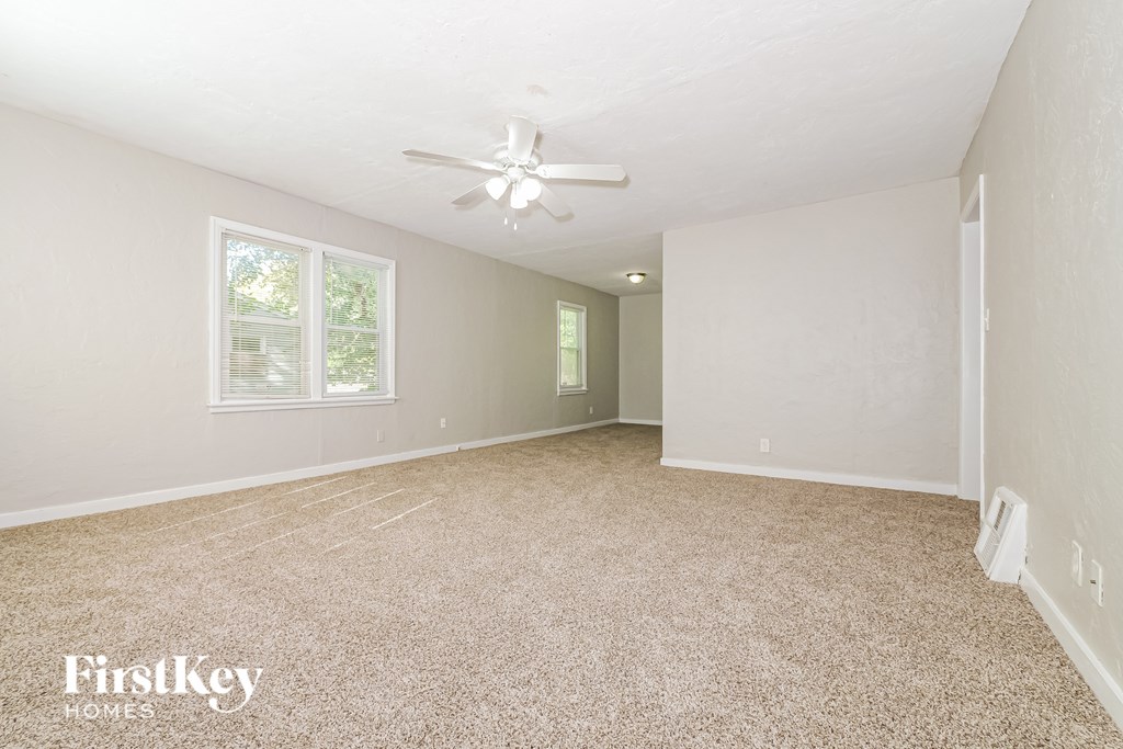 A spacious room with a carpeted floor, a ceiling fan, and a window letting in natural light.