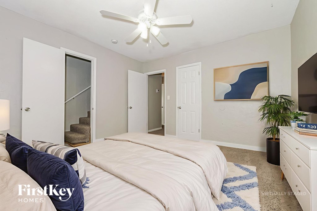 A bedroom with a large bed, a ceiling fan, and a painting on the wall.