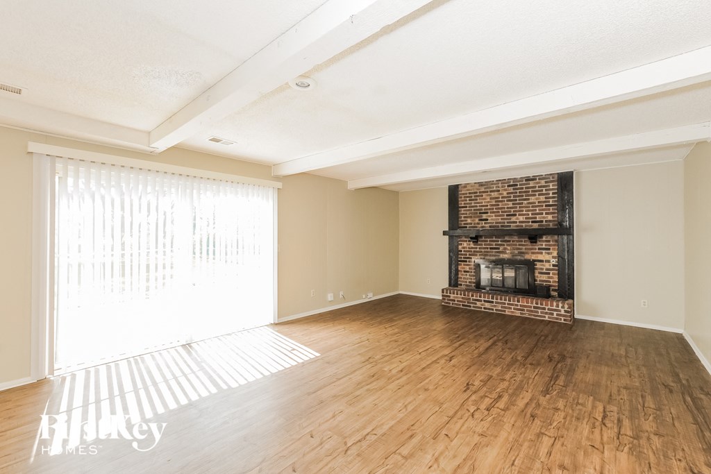 an empty living room with a brick fireplace and wooden floors