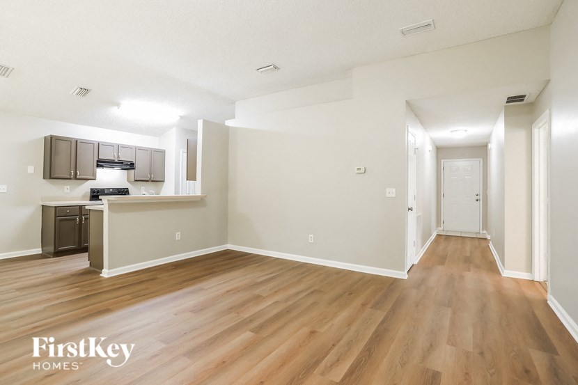 the living room and kitchen of an apartment with hardwood flooring and white walls