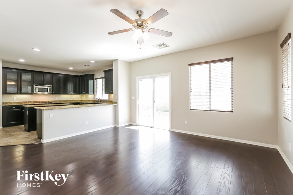 A spacious room with a ceiling fan and dark wood flooring.