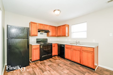 A kitchen with orange cabinets and a black fridge.