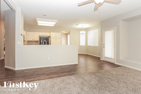 A spacious living room with a kitchen in the background and a fan on the ceiling.