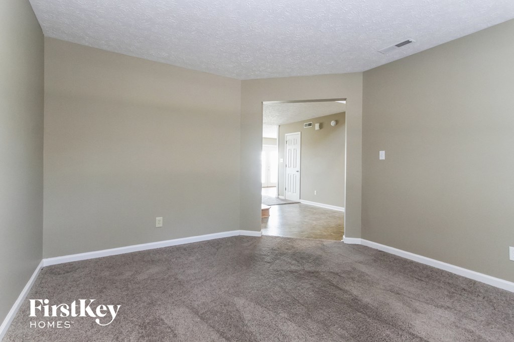 an empty living room with carpet and a door to a hallway