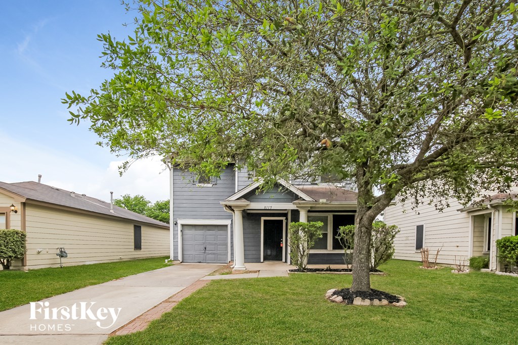 a blue house with a tree in the yard and a sidewalk