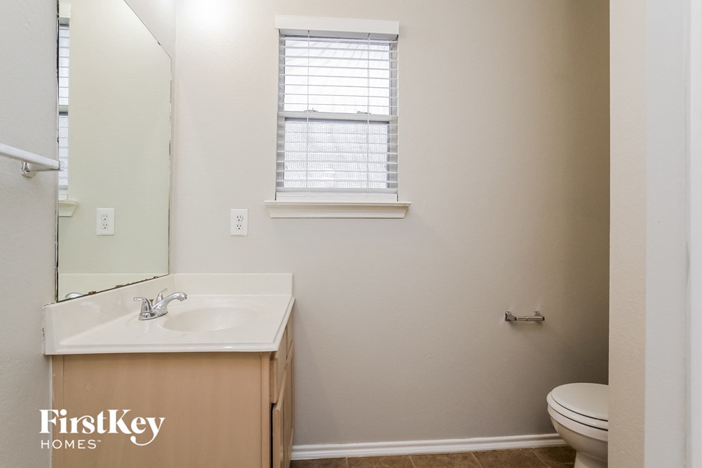 a bathroom with a toilet sink and mirror and a window
