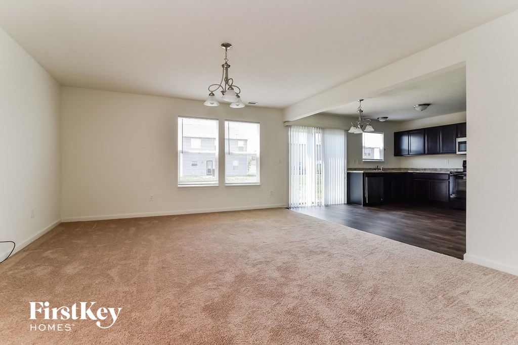 A spacious living room with a carpeted floor and a chandelier hanging from the ceiling.