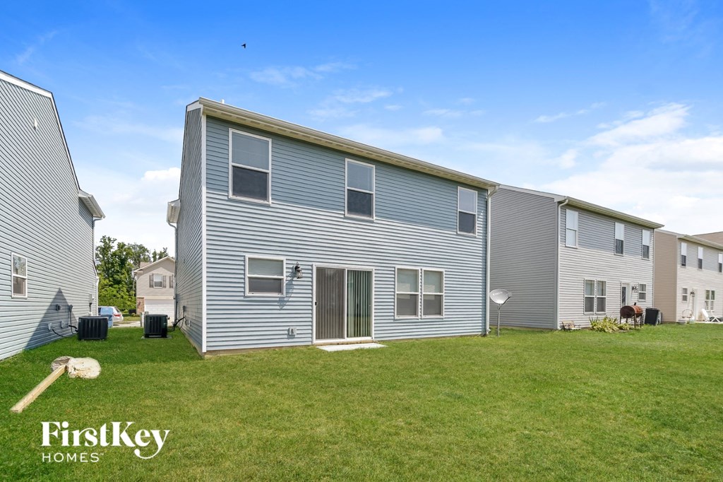 A FirstKey homes sign is on a grassy area in front of a grey house.