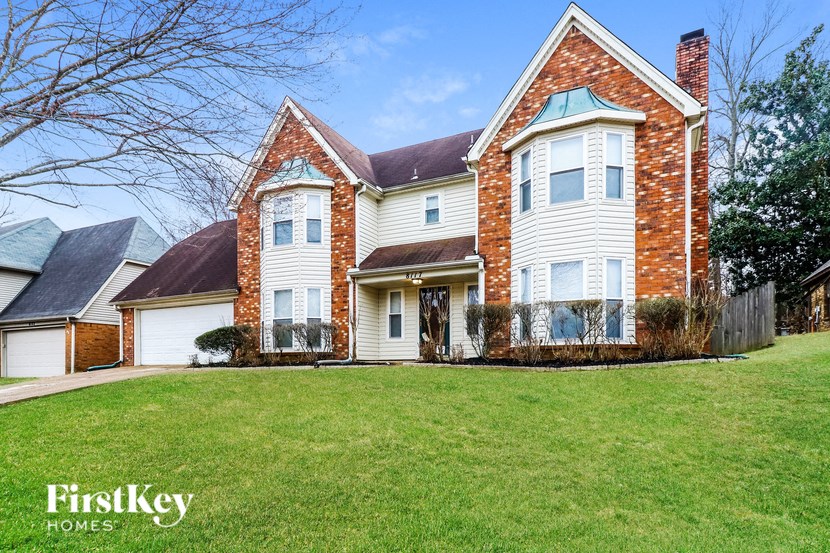 A large brick house with a white garage door and a green lawn.