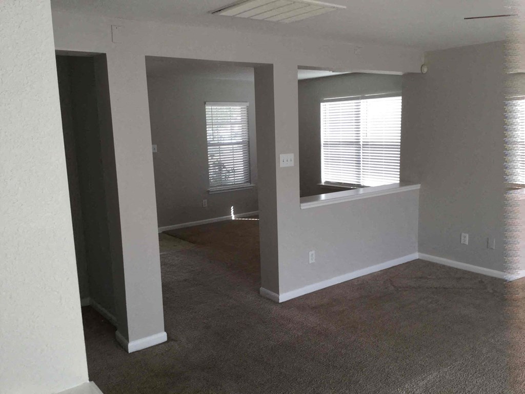 A room with a carpeted floor and two windows with blinds.