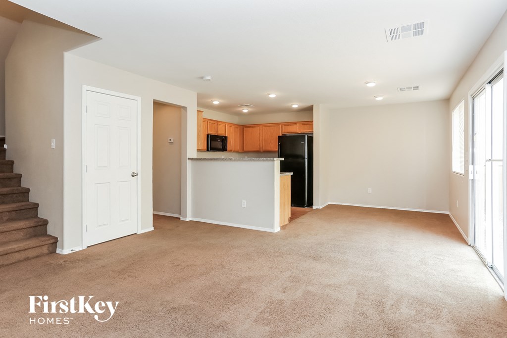 an empty living room with a kitchen in the background