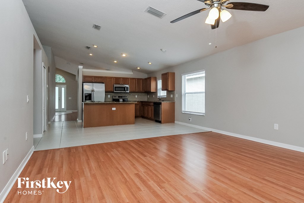 an empty living room and kitchen with wood flooring and a ceiling fan