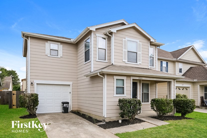 a beige house with white garage doors and a lawn