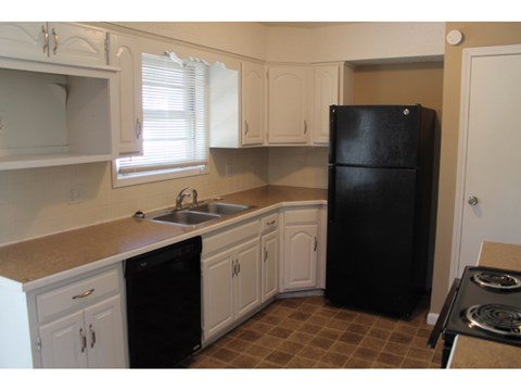 A black refrigerator sits in a kitchen with white cabinets.