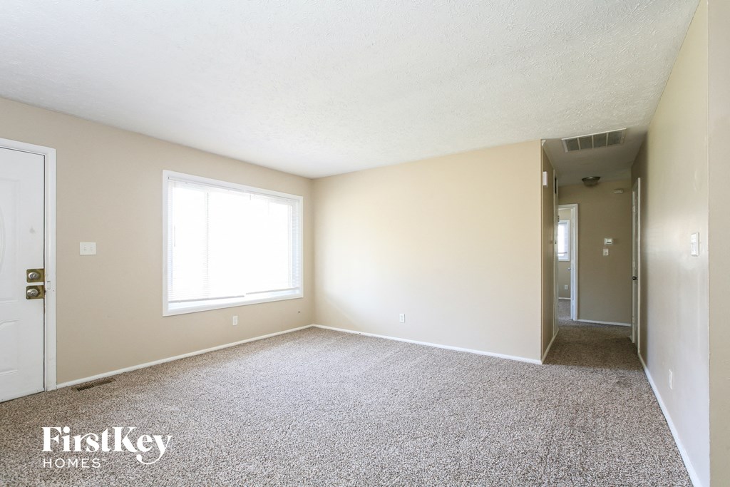 an empty living room with carpet and a door to a hallway