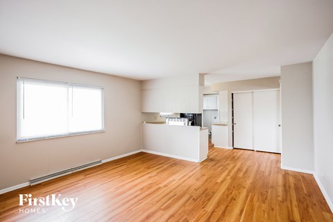 A room with wooden floors and white walls, with a window on the left side.