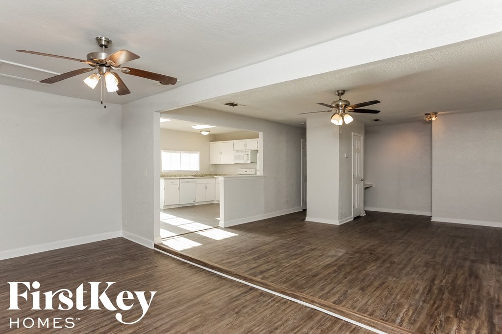 an empty living room with two ceiling fans and a kitchen