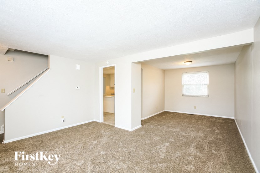 an empty living room with white walls and carpet and a staircase