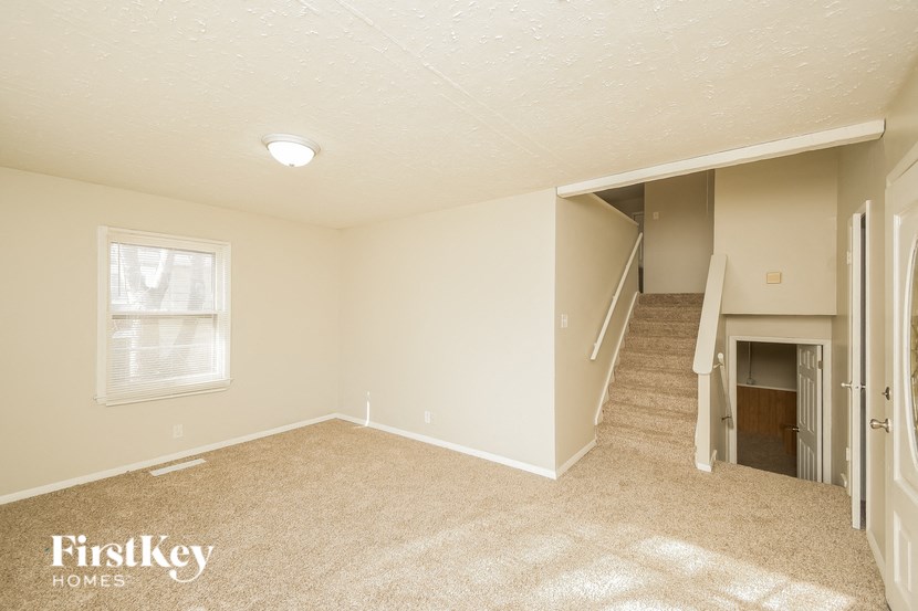 A room with a carpeted floor and a stairway leading to another room.