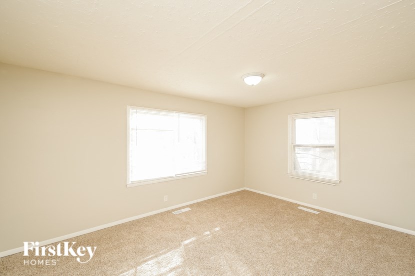 A room with a carpeted floor and two windows.
