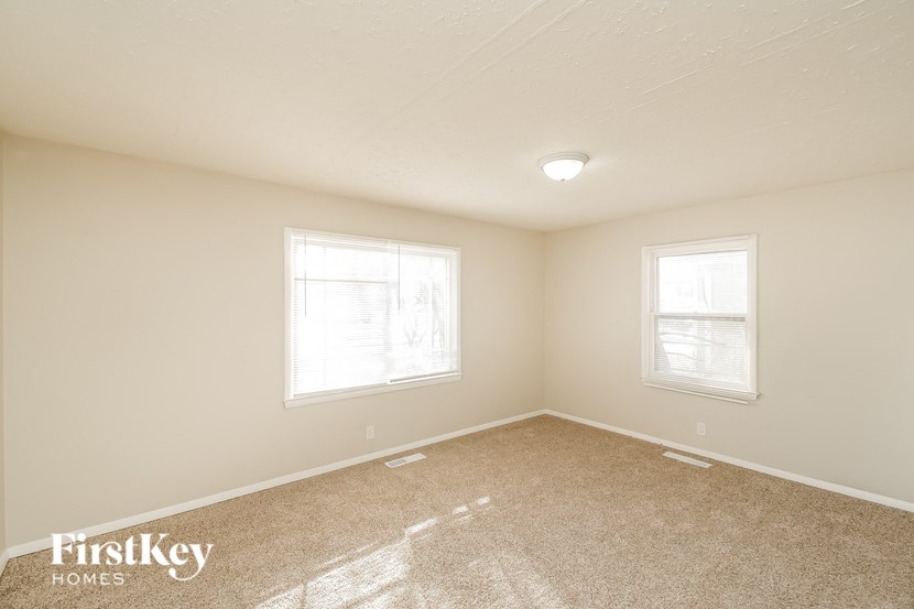 A spacious empty room with two windows and a carpeted floor.