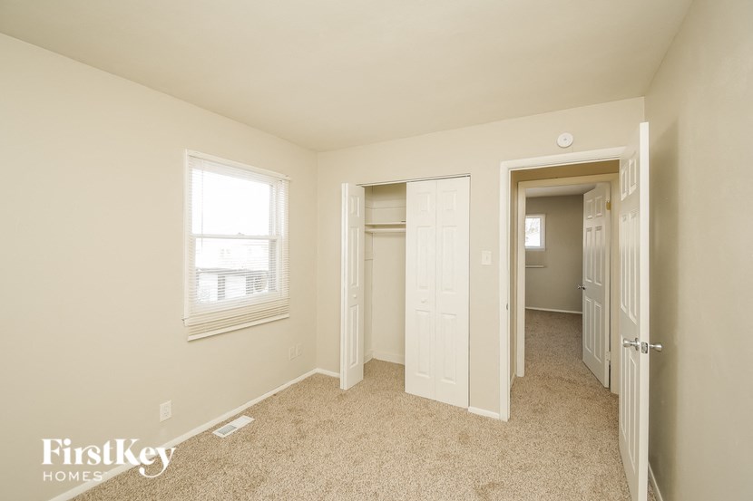A carpeted room with a window and a door leading to another room.