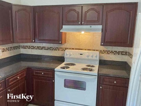 A kitchen with a white stove top oven and brown cabinets.