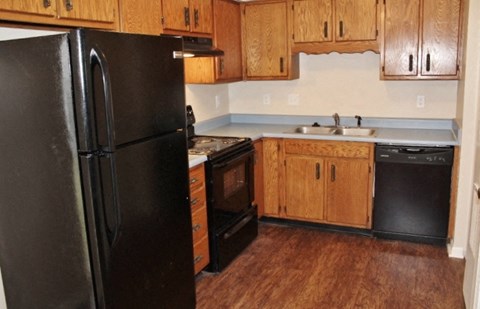 A black refrigerator stands in a kitchen with wooden cabinets and a stove.