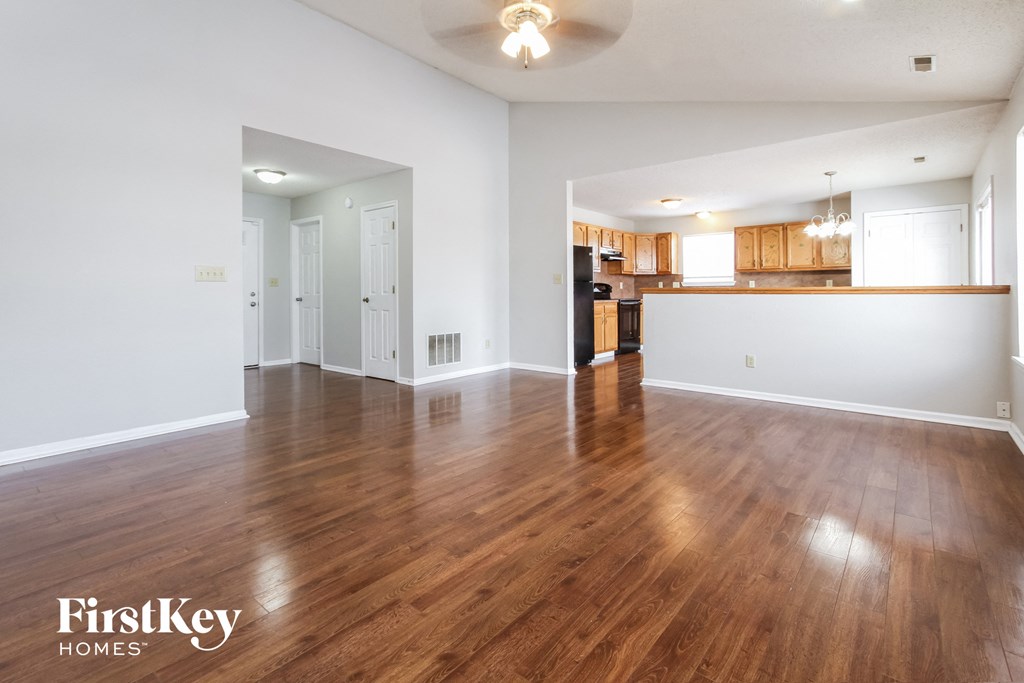 an empty living room with wood flooring and a kitchen