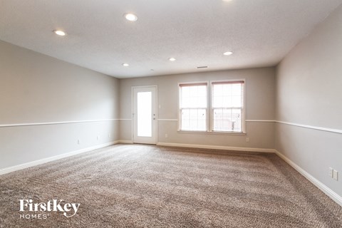 A spacious room with a carpeted floor and two windows.