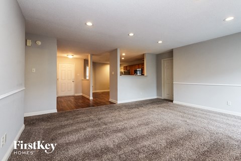 A spacious room with a carpeted floor and a kitchen area in the background.