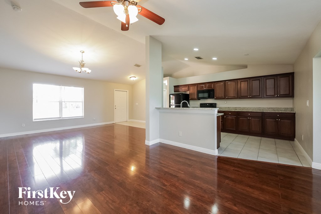 an empty living room and kitchen with wood flooring and a ceiling fan