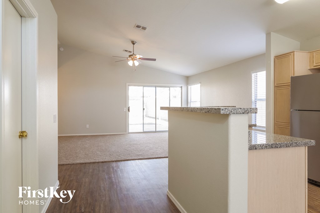 an empty living room with a kitchen and a ceiling fan