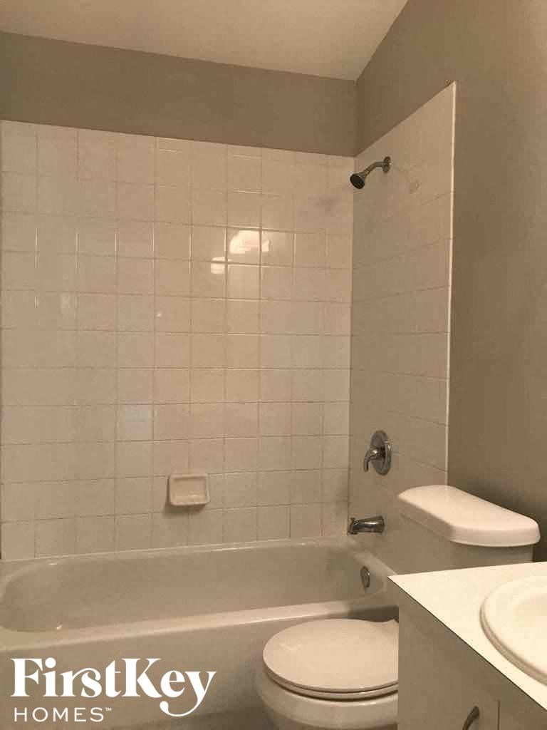 A white toilet sits next to a white sink in a white tiled bathroom.