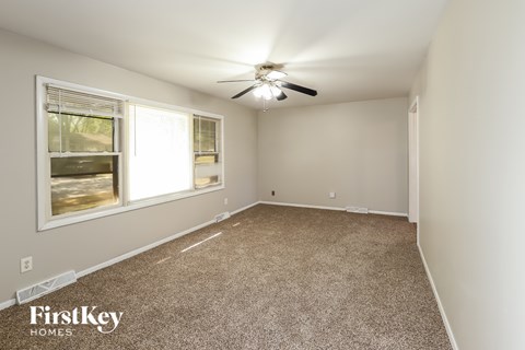 A room with a carpet floor, a ceiling fan, and a window showing an outdoor view.