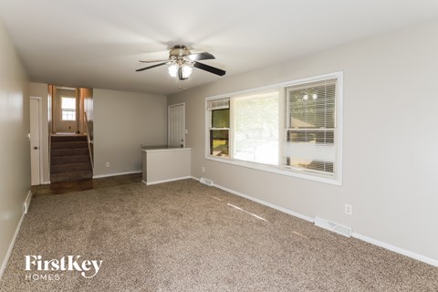 A spacious room with a carpeted floor, a ceiling fan, and a window with blinds.