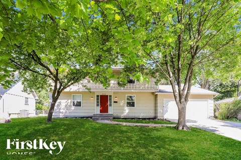 A white house with a red door is surrounded by green trees.