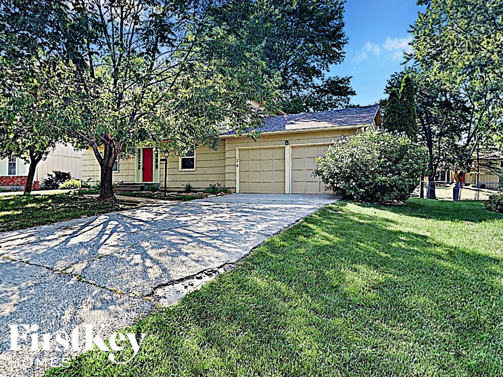 A house with a red door is surrounded by trees and has a driveway.