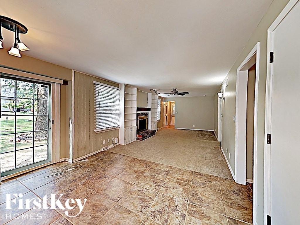 A large empty room with a tiled floor and a sliding glass door leading to a backyard.