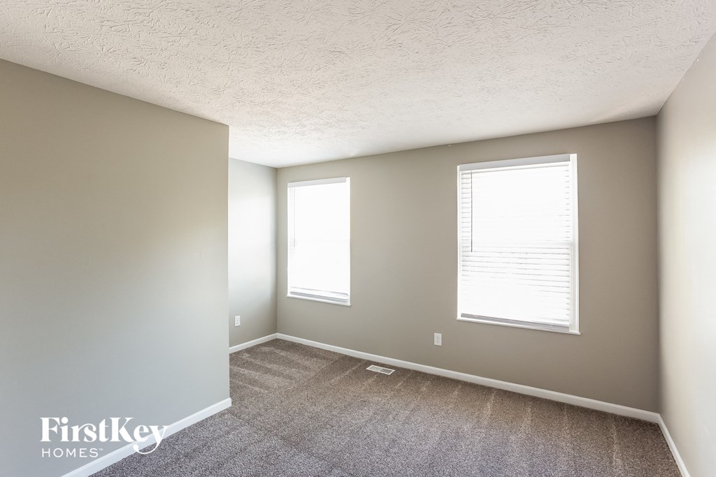 an empty room with a carpet and two windows