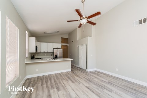 A spacious room with a ceiling fan and a kitchen area in the background.