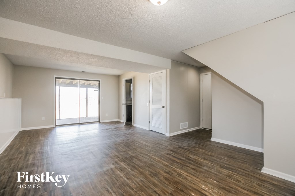 the living room and dining room of an apartment with wood flooring and white walls