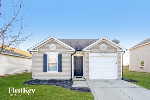 a beige house with two white garage doors and a sidewalk