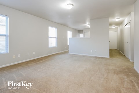 the living room and dining room of an apartment with carpeting and white walls