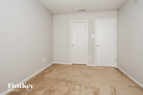 a bedroom with white walls and carpet and two doors