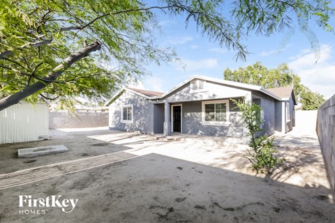 A house with a grey exterior is surrounded by a dirt lot and trees.