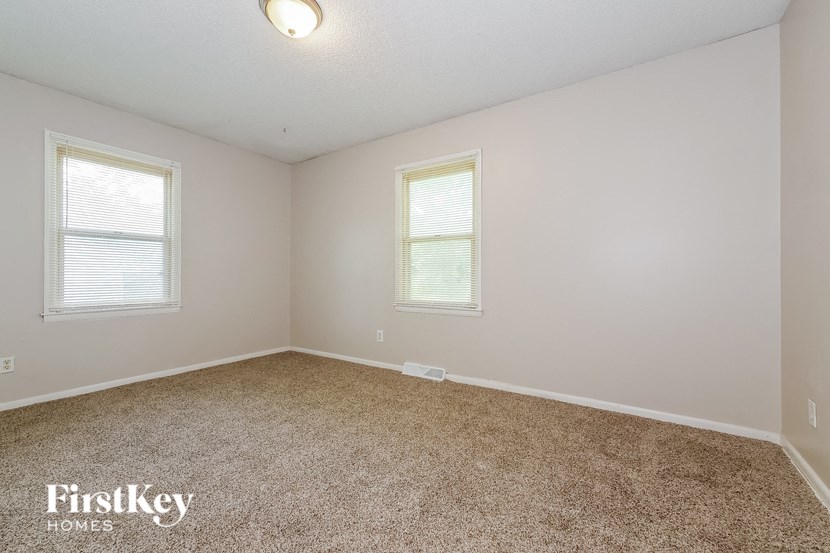 an empty bedroom with two windows and a carpeted floor