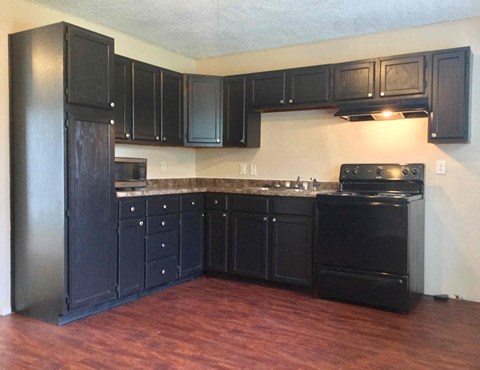 an empty kitchen with black cabinets and a wood floor