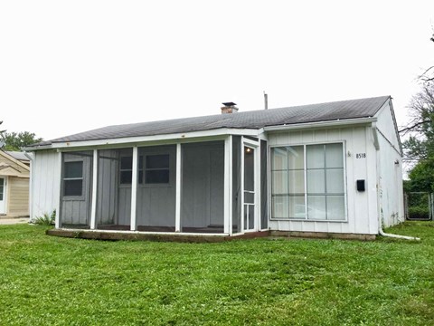 a small white house with a porch and a lawn