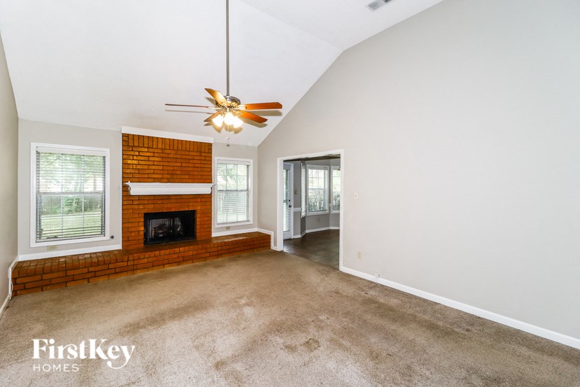an empty living room with a brick fireplace and a ceiling fan